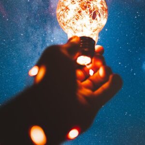 Une main tendue vers le ciel entourée d'une guirlande lumineuse & au bout une ampoule allumée illustrant la pleine conscience