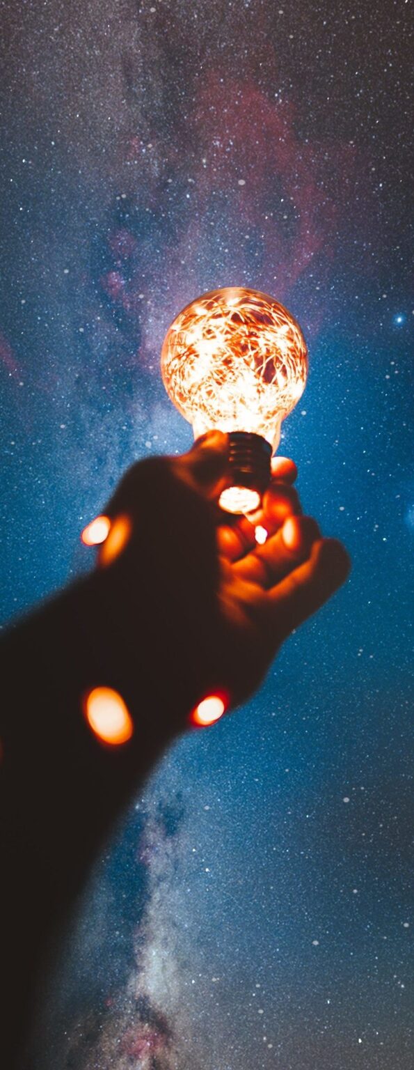 Une main tendue vers le ciel entourée d'une guirlande lumineuse & au bout une ampoule allumée illustrant la pleine conscience