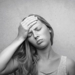 Une jeune femme se tient le front et fronce les sourcils comme si elle se plaignait de douleurs migraineuses